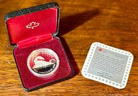 Photo of silver proof dollar coin in black clamshell case with red velvet interior, alongside a certificate card.