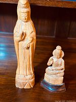 Photo showing both carved wooden idols together on a wood surface, highlighting size difference and detail.