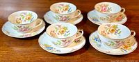 All five tea cups and saucers arranged on a wooden surface showing matching floral pattern and gilded decoration.