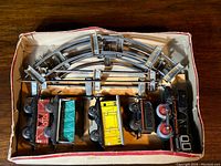 Top-down view of train set in box showing locomotive, wagons and metal curved track pieces.