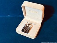 Front view of the pendant necklace in box showing silver floral motif with MOP tips on a rectangular pendant plate.