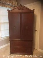 Full front view of the mahogany two-door, two-drawer armoire against a wall near window with curtain.