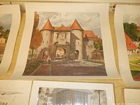 Close-up of a watercolor reproduction print depicting a historic castle-like building with red roofs and archways, likely one of the Paul Burruss prints measuring 19" x 19".