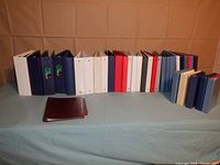 Full view of all 35 binders in multiple sizes and colors placed in a line on a light blue cloth surface