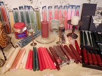 Wide view of assorted candles including tapers, pillars, and votives alongside several candle holders and candle packaging.