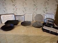 Full lot of cookware displayed on table including pans, toaster, drip pans, splash screen, and baking trays.