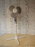 Full view of the SMC floor fan standing on a four-legged pedestal with a decorative floral wallpaper in background.