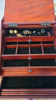 Open large wooden jewelry box displaying black felt-lined compartments and assorted costume jewelry pieces including earrings and pins.