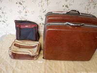 Lot containing two hard cased Samsonite luggage and two soft sided shoulder bags shown side by side on a bed with floral wallpaper background.