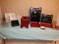 Black, white, and red plastic trays and organizers arranged on a blue tablecloth, showing stackable letter trays and various sized sorters.
