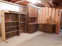 Full view of incomplete shelving units in a basement showing multiple pieces arranged adjacently including hutches and base cabinets with doors.