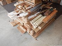 Image showing a large pile of various wood pieces including painted white boards, natural wood slabs, several turned legs and spindles, and carved posts.