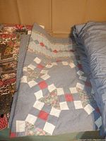 Photo shows all three items folded and stacked: a festive Heritage Quilts snug sack, a multi-color patchwork quilt, and a solid blue quilted duvet.