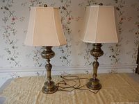 Pair of vintage brass table lamps with octagonal ivory shades placed on a table against wallpapered wall.