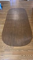Four large oval-shaped dining table pads with wood grain top and felt underside laid out on hardwood floor in folded position showing wood texture and fold lines.
