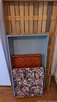 Wood lattice tray standing vertically, with light blue paper-covered drawer organizer and brown bamboo serving tray inside it. Floral fabric organizer folded and placed in front.