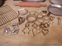 Photo showing cooling rack, various metal tart pans, cookie cutters in heart, star, flower, and geometric shapes, dough cutter, and part of rolling pin.