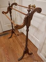 Side angle view showing the rolled wood ends, spindle tops, and curved feet of the wooden quilt rack.