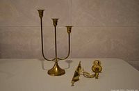 Photo of three-arm brass candle holder and brass wall-mounted candle holder on a countertop.