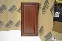 Medium sized solid wood cabinet door with raised panel and decorative edges, dark brown finish.