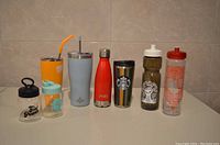 All eight travel bottles side by side on a tiled surface, showing size, color and lid styles.