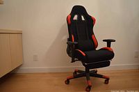 Full view of black and red gaming chair with lumbar support pillow on wooden floor.
