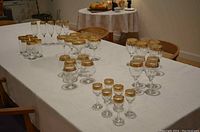 Wide view of entire set of gold-rimmed glasses arranged on table, showing variety and quantity of glasses.