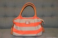 Front view of Kate Spade purse showing orange and beige stripes with leather handles and tassels.