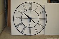 Full view of the large metal wall clock showing black Roman numerals and clock hands against a white background, measuring 45 inches in diameter.