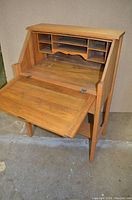 White oak secretary desk opened showing six cubby compartments and a central shelf inside.