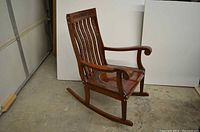 Right angled side view of the wooden rocking chair showing the curved armrest and flat runners.