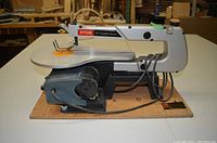 Side view of Ryobi 16" variable speed scroll saw with plywood base showing saw arm, motor, and cord.