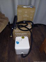 Dupray Neat steam cleaner main unit with attached hose, standing on floor beside original box and accessories box.