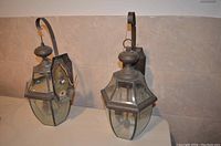 Two exterior hanging lantern lamps mounted on curved wall brackets, one lamp door open showing inside.