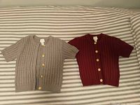 Photo showing both beige and red short-sleeve cable knit cardigans with gold buttons on striped background.
