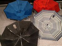 Four opened umbrellas showing colors and patterns: solid blue, solid red, solid black, and blue and white stripes.