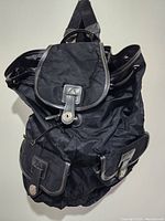 Front view of a black nylon backpack showing two front pockets with buckle closures and the main flap with buckle strap.