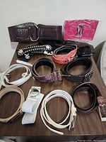 Top view of 12 decorative belts laid out on table showing variety in color, texture, width, and buckle style.