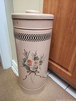 Full view of the beige metal bin with floral design and cut-out detail near the rim