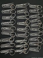 Top-down view of 30 metal curtain clips arranged in rows on a dark background showing their design and attached rings.