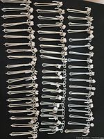Full view of the lot showing multiple identical metal curtain clips with attached white plastic rollers, arranged in rows on black background.