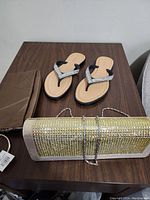 Pair of black and rhinestone sandals next to brown and rhinestone clutch handbags on wooden surface