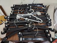 Overview of the lot showing mostly black plastic hangers with clips and a few white plastic hangers on a table.