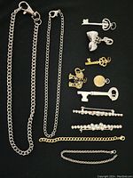 Full view of lot with chains, key pendants, heart-shaped pendant, hair clips, and gold chain bracelet on black background.