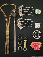 Full view of all jewelry items including necklace, pendant, rings, hair clips, and dress pins on black background