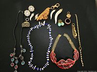Overview showing the full collection of jewelry with necklaces, earrings, pendants, chain links, and a ring on a black background.