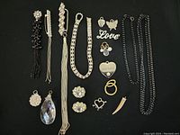 Full view of assorted jewelry items arranged on black surface including chains, rings, earrings, and pendants.