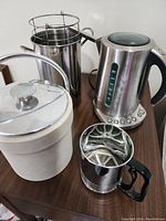 Image showing all four items together on a wooden surface: electric kettle, French press, sifter, and ice bucket.