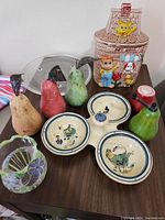Full view of lot showing ceramic pear mashers, ceramic cookie jar, ceramic bowls, metal lid on dark wood table