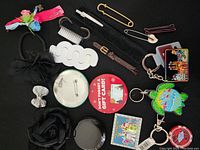 Full view of mixed accessory items including hair ties, clips, pins, keychains and other small items on black background